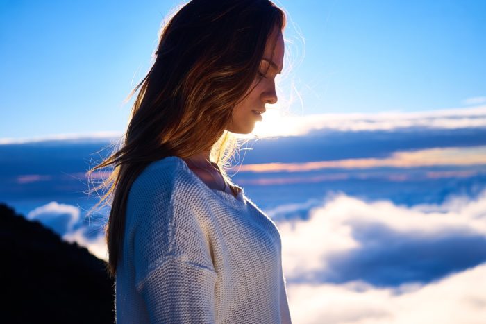 空と雲をバックにうつむく女性